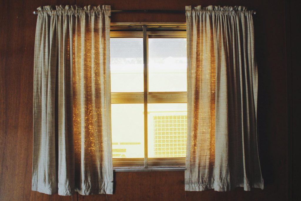 Warm sunlight streaming through fabric curtains in a wooden interior setting.